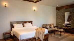 A bedroom with a large wooden bed, a wooden nightstand, a sofa, a small table, and a stone wall. - Palette Hotel Amritsar by Checkin (Amritsar)