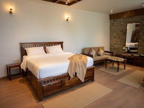 A bedroom with a large wooden bed, a wooden nightstand, a sofa, a small table, and a stone wall. - Palette Hotel Amritsar by Checkin (Amritsar)