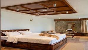 A spacious bedroom with a large bed, wooden headboard, and a stone wall. - Palette Hotel Amritsar by Checkin (Amritsar)