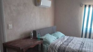 A bedroom with a bed, a desk, and a window with blinds.