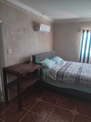 A bedroom with a bed, a desk, and a window with blinds.