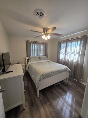 A bedroom with a bed, a desk, a ceiling fan, and a window with curtains.
