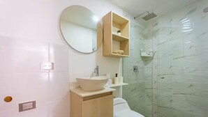 Ein Badezimmer mit rundem Spiegel, Waschbecken, Toilette und einer Duschkabine aus Glas.
