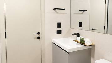 A modern bathroom with a white door, a sink with a mirror above it, and a toilet.
