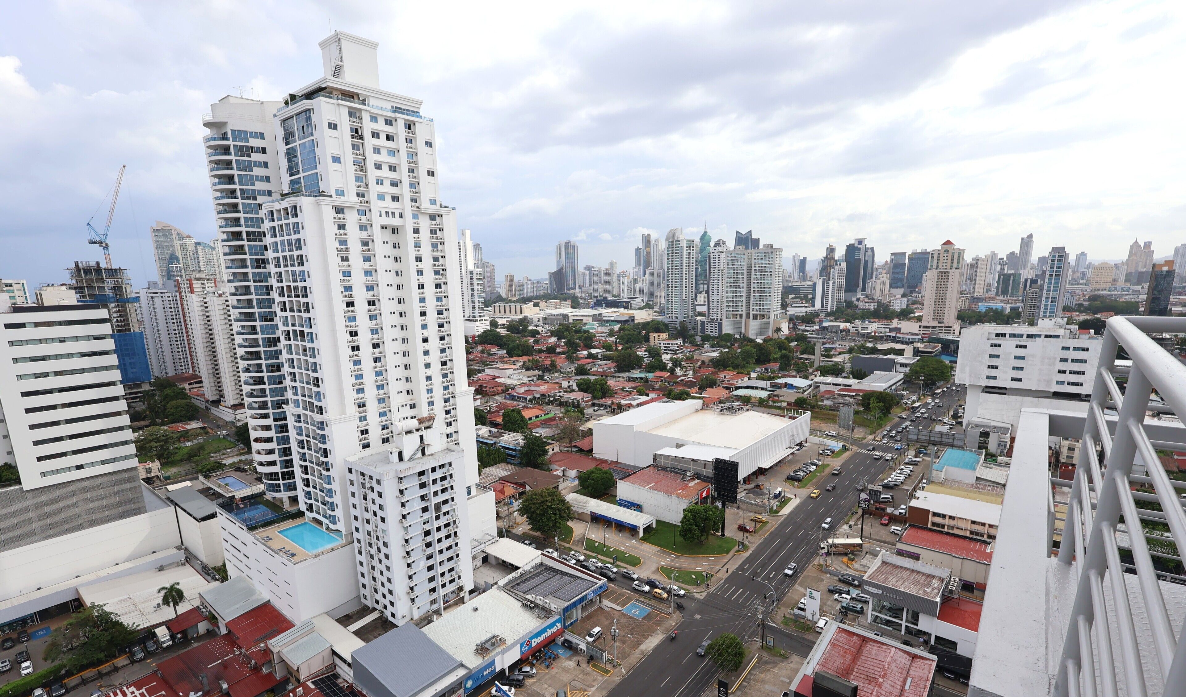 A high-rise building with multiple floors and balconies, surrounded by other buildings and a busy street.