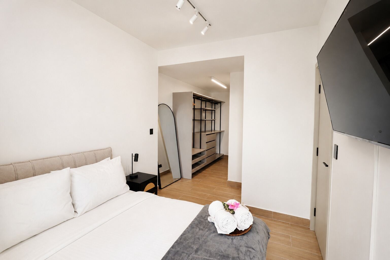 Un dormitorio moderno con cama, mesita de noche y un taburete con toallas.