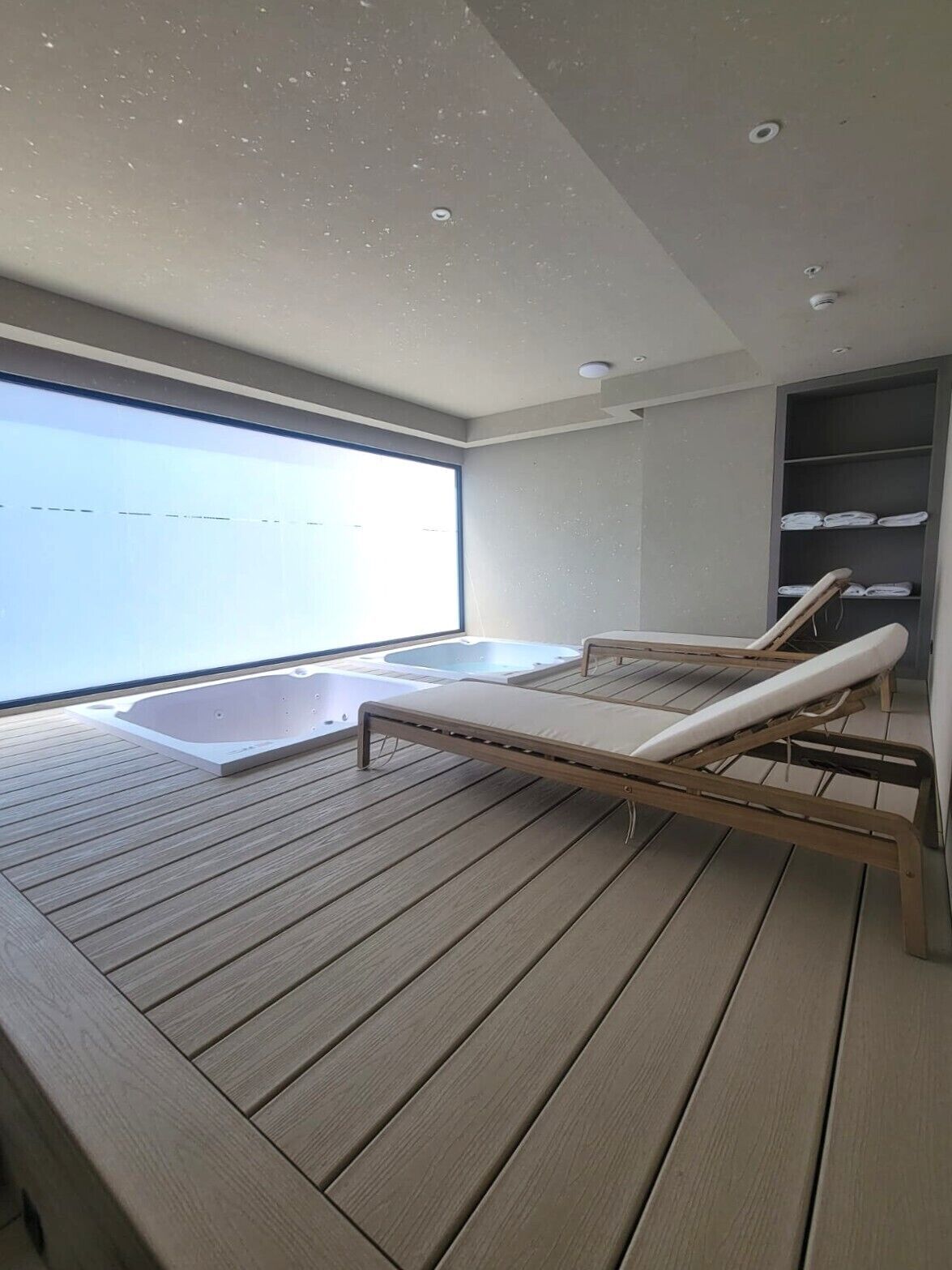A modern outdoor lounge area with a wooden deck, a hot tub, and a seating area with cushions.