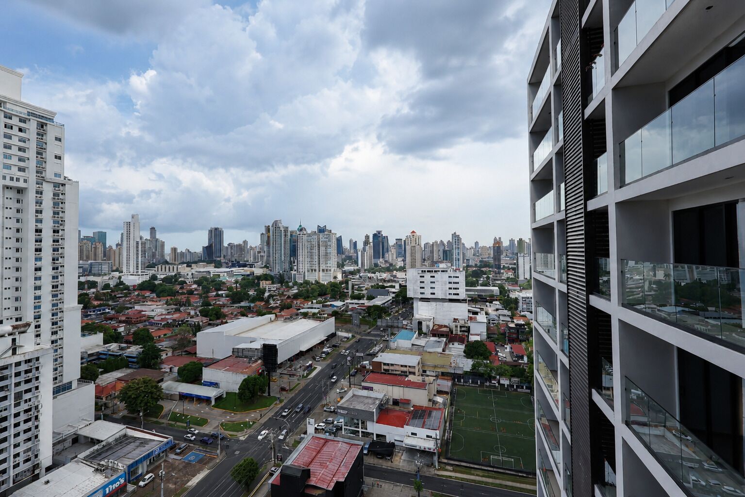 Un edificio de gran altura con varios pisos, amplias ventanas y vista a un paisaje urbano con diversos edificios y un campo deportivo.