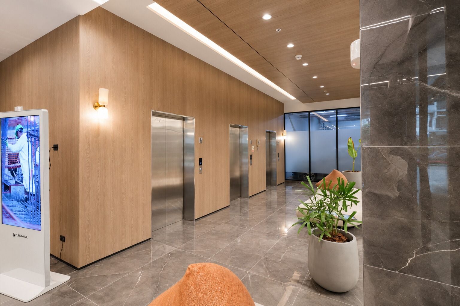 A modern lobby with wooden paneling, a digital display, and a potted plant.