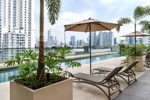 A rooftop pool area with lounge chairs, a large umbrella, and a city skyline view. - The Hub by Boutique Apartments (Panamá)