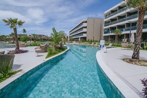 Ein Swimmingpool mit Liegestühlen und Palmen, umgeben von einem modernen Gebäude mit Balkonen.