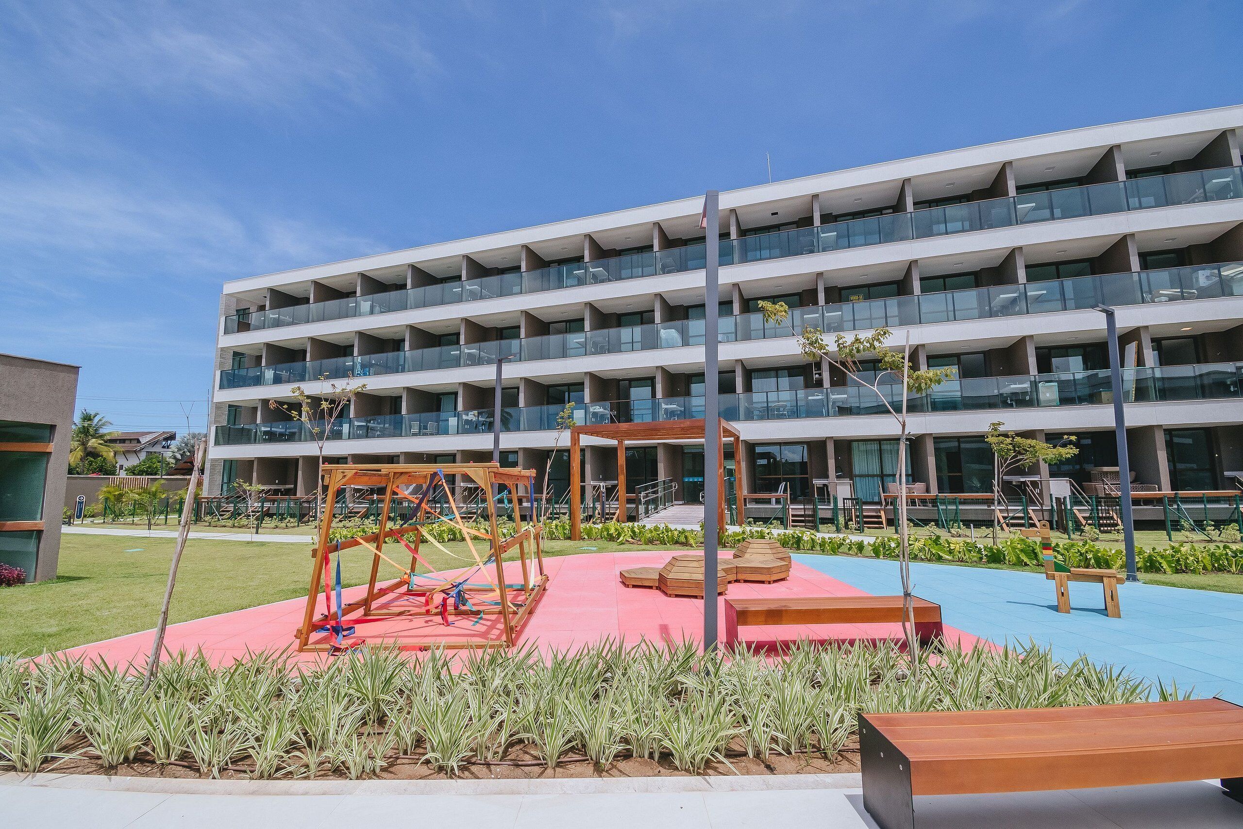 A multi-story building with a rooftop terrace and a playground area with swings and seating.