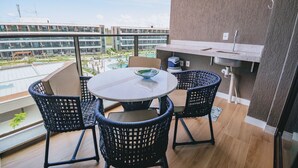Varanda com mesa redonda e quatro cadeiras, pia pequena e vista para uma piscina e edifícios.