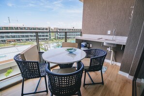 Ein Balkon mit rundem Tisch, vier Stühlen, einem kleinen Waschbecken und Blick auf einen Swimmingpool und Gebäude.