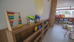 Espaço infantil com prateleiras de madeira, ábaco colorido, um balde e um baú de brinquedos.