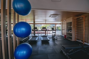 Ein Fitnessraum mit Trainingsgeräten, darunter Laufbänder und ein Rudergerät, sowie große, blaue Trainingsbälle.
