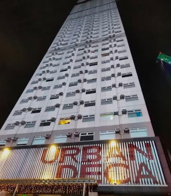 Een hoog gebouw met meerdere airconditioners op de gevel, een groot verlicht bord onderaan en een groen licht aan de rechterkant.