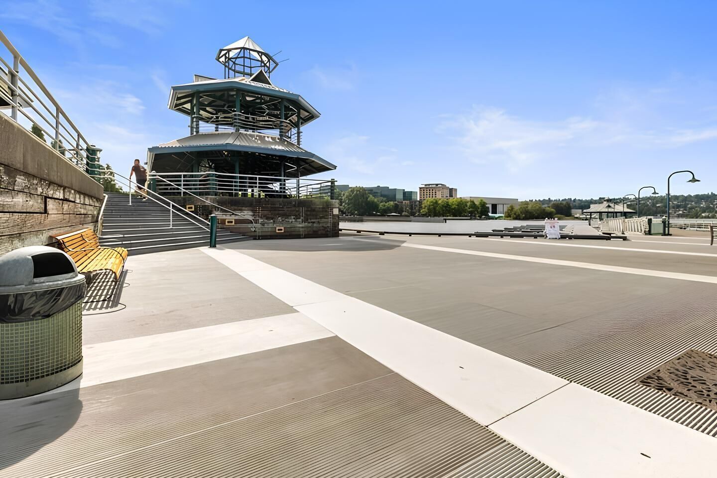 A waterfront promenade with a lookout tower, benches, and a trash can.
