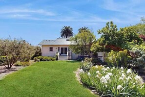 Une maison avec une pelouse bien entretenue, un porche à l’avant et diverses plantes et arbres.