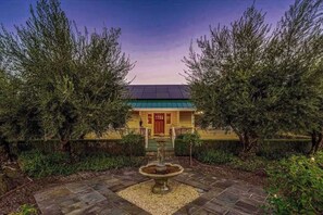 A house with a green roof, a red door, and a stone fountain in the garden.
