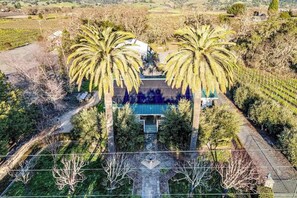 Vue aérienne d’une propriété avec un bâtiment central, entouré de palmiers et d’un jardin aménagé.