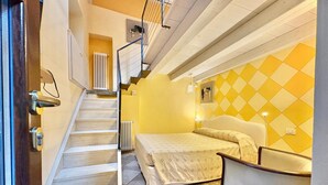 A hotel room with a bed, a chair, a desk, a radiator, and a staircase. - Charming Suite in the Heart of Cannero Riviera, Lake Maggiore (Cannero Riviera)