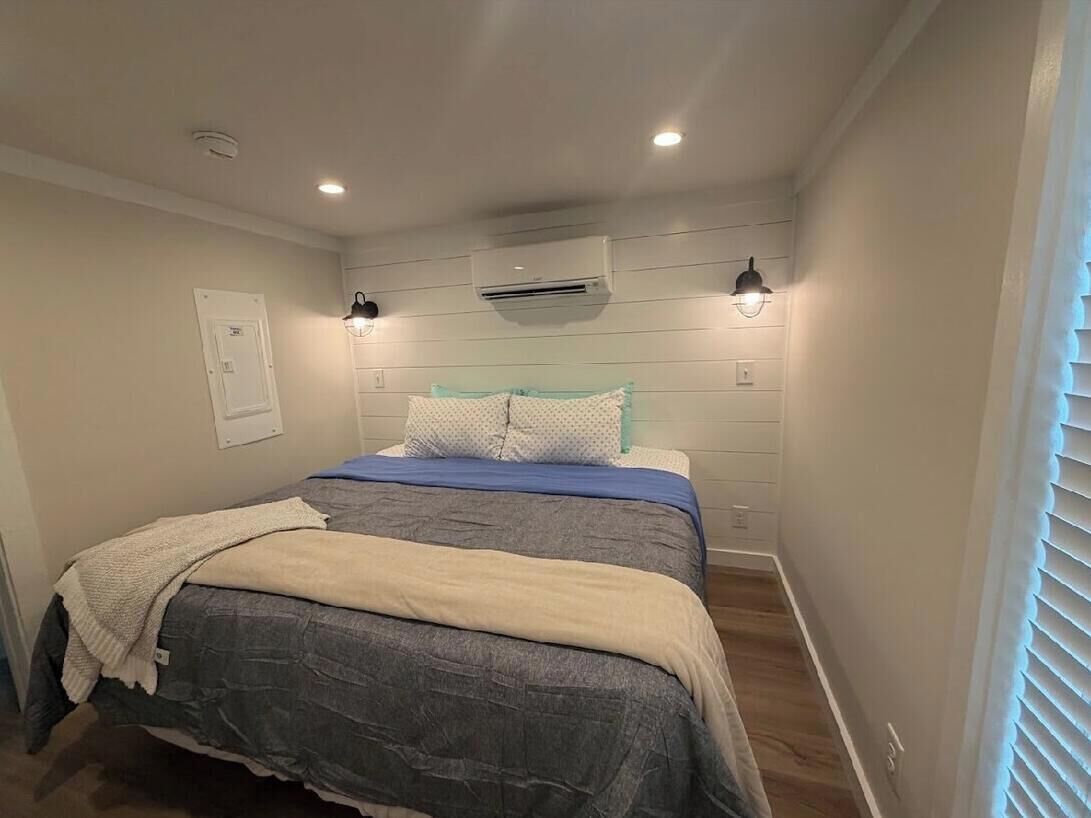 Een slaapkamer met een bed, twee wandlampen, een airconditioning en een deur.