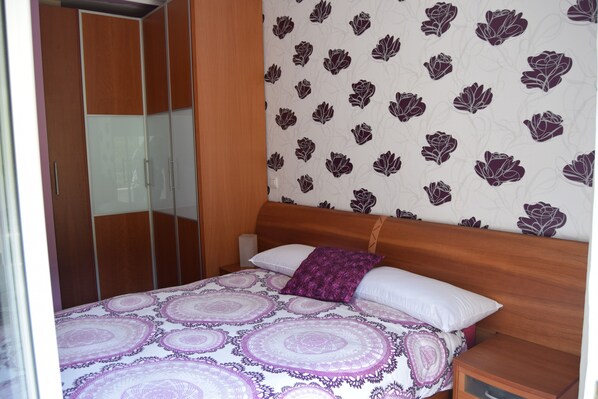 A bedroom with a bed, wooden headboard, a nightstand, a mirror, and a wardrobe.