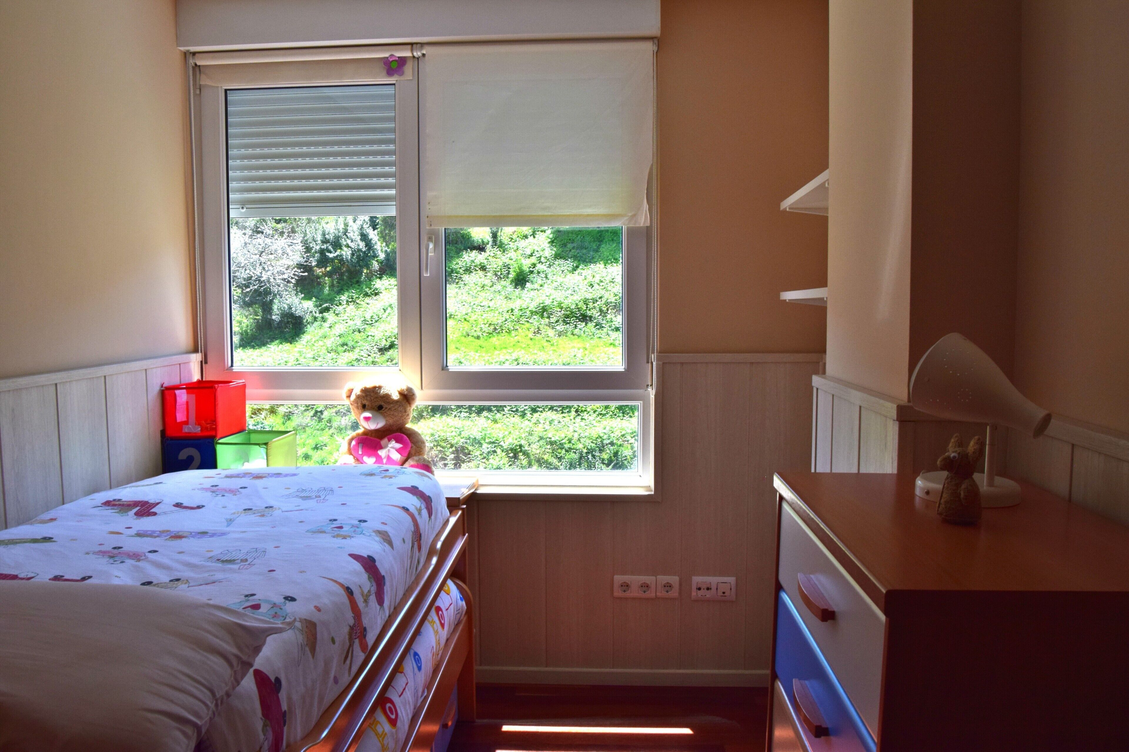 Un dormitorio con cama, ventana, cómoda y un oso de peluche.