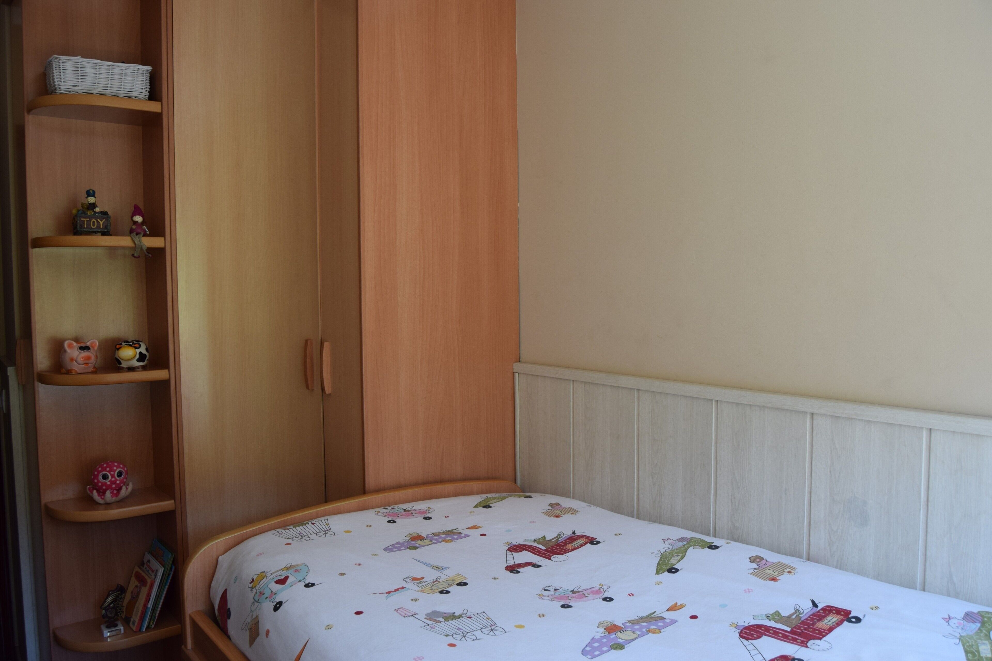 Un dormitorio con una cama, un armario de madera y estantes con juguetes y libros.