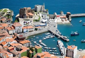 An aerial view of a coastal town with historic buildings, a fortified structure, and a marina with boats.