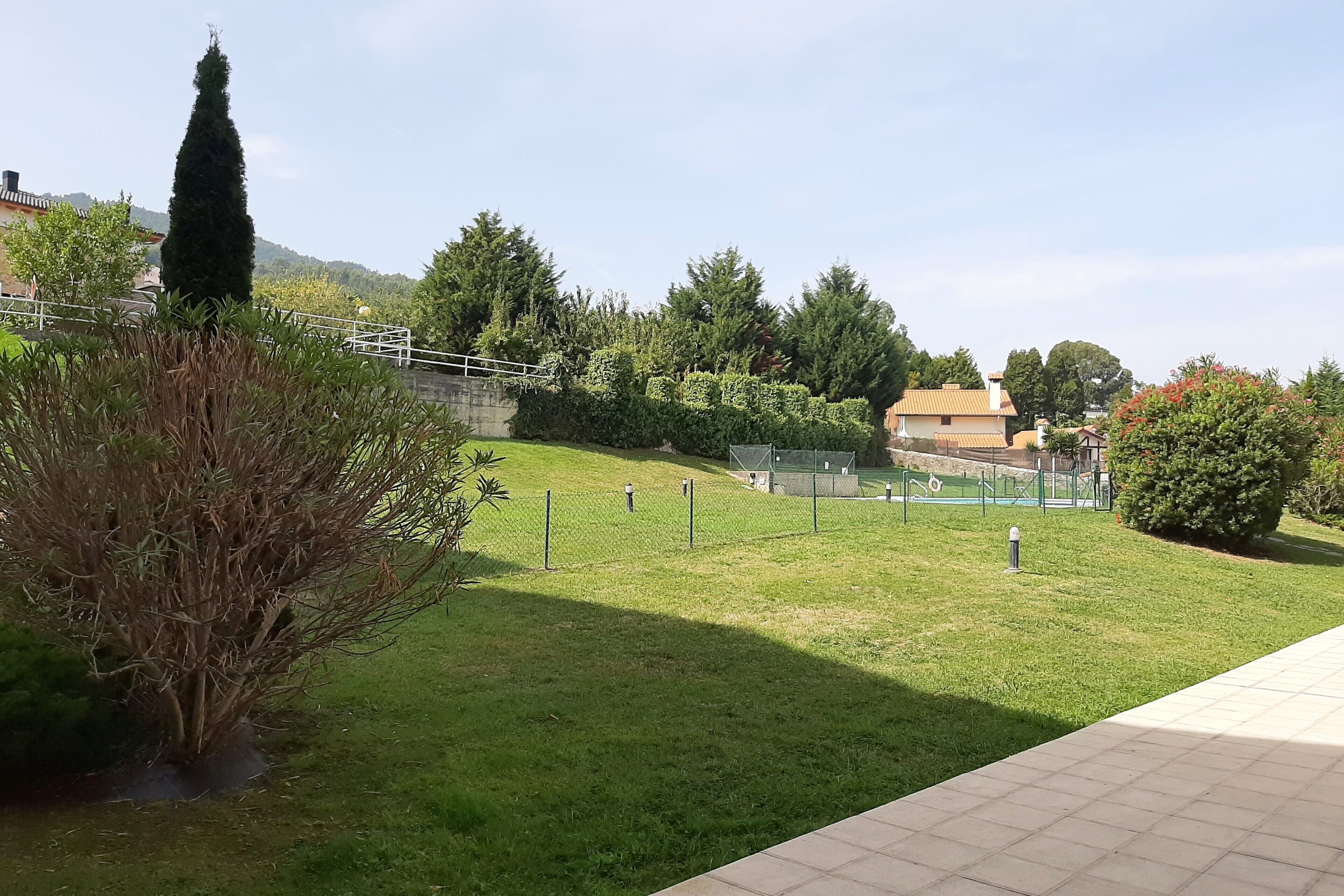 A grassy area with a fence, a tall tree, and a building in the background.