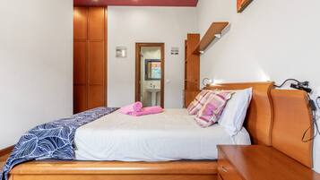 Een slaapkamer met een houten bed, een nachtkastje, een spiegel en een deur naar de badkamer.