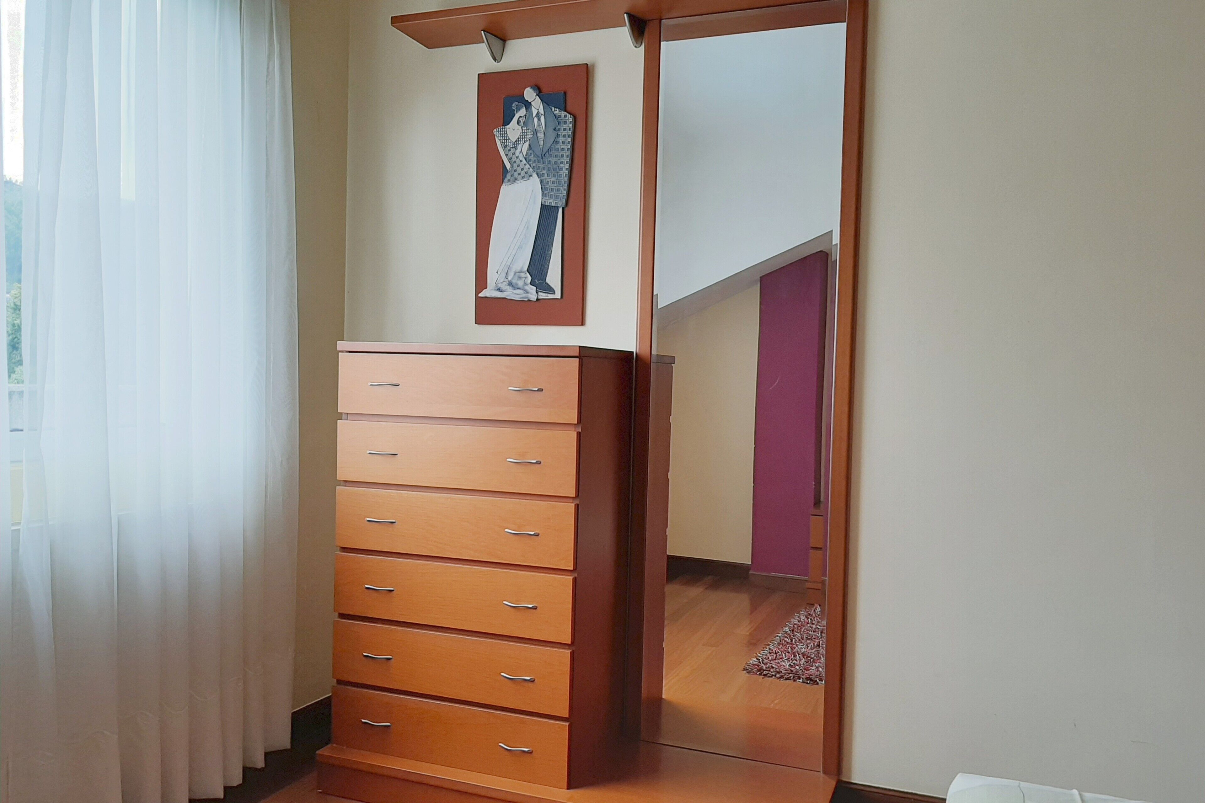 A room with a wooden dresser, a framed artwork on the wall, and a view of a staircase.