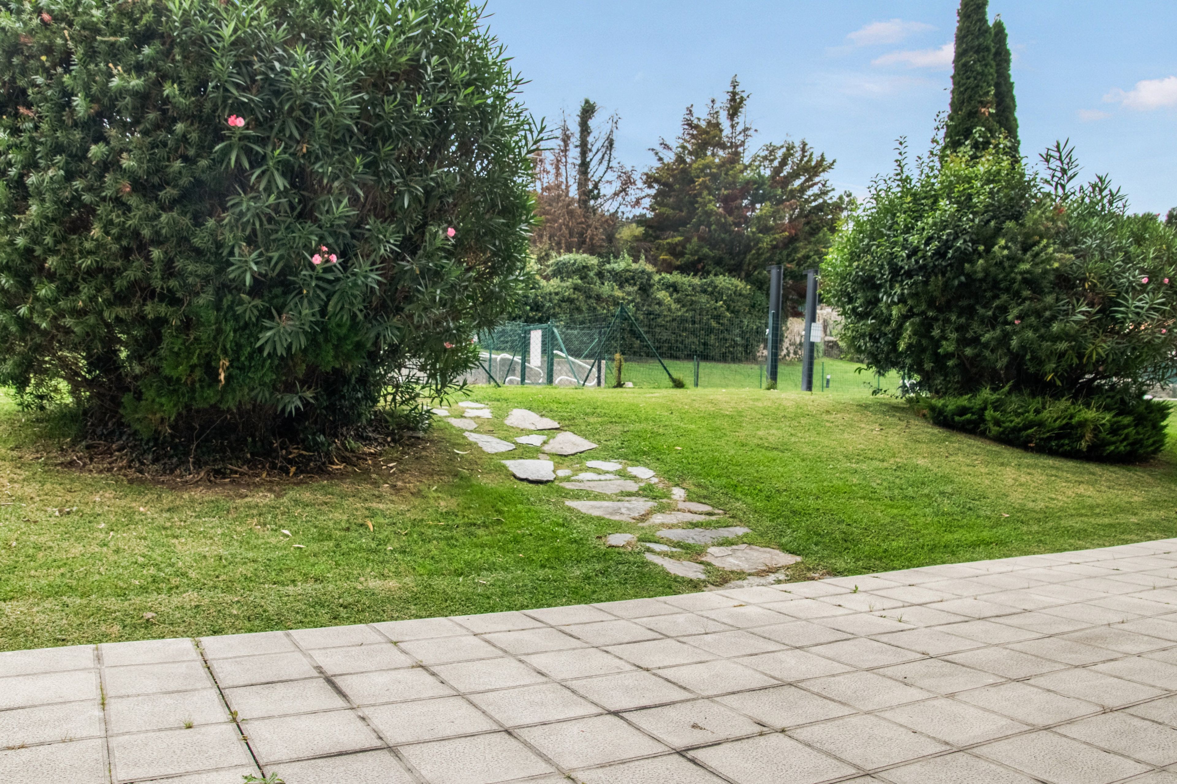 A paved pathway leading through a well-maintained garden with various shrubs and a clear sky.