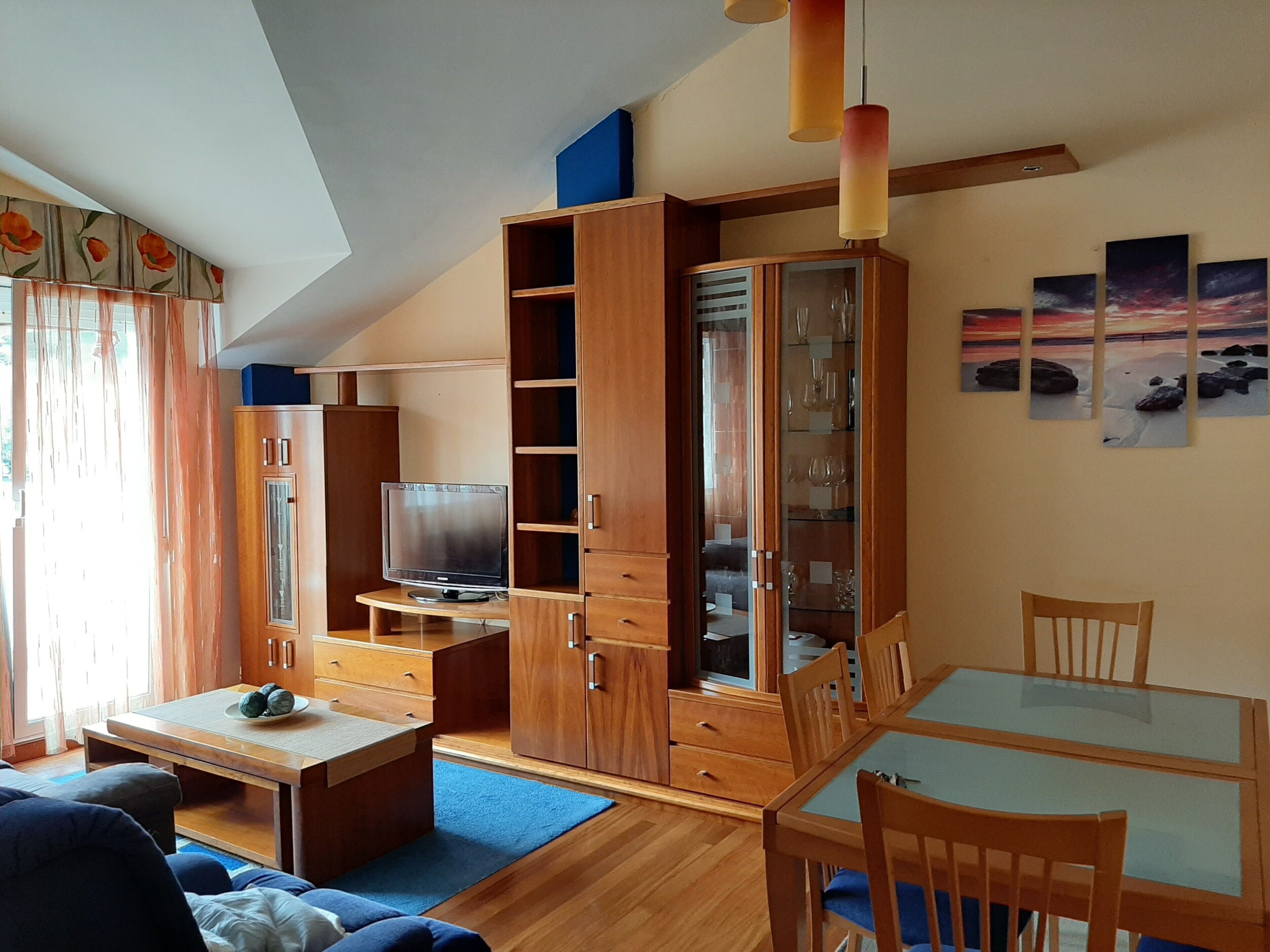 A living room with a TV, wooden cabinets, a dining table, and a blue rug.