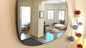 Um espelho reflete um quarto com uma cama, um sofá, uma mesa de centro e um quadro na parede.