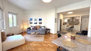 Uma sala de estar moderna com sofá, mesa de jantar e cozinha ao fundo.