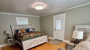 A bedroom with a bed, a chair, a nightstand, a lamp, and a door.