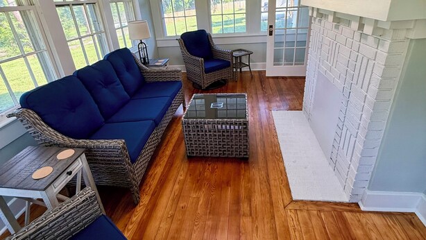 A room with a blue sofa, wicker chairs, a small table, and a fireplace.