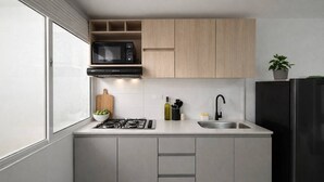 A compact kitchen with a gas stove, a black microwave, a sink, and wooden cabinets. - Comuna 13 Urbana | 1-minute walk to the metro + Coworking (Medellín)