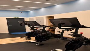 Un gimnasio con bicicletas estáticas, una puerta con letrero de salida de emergencia y una pared azul.