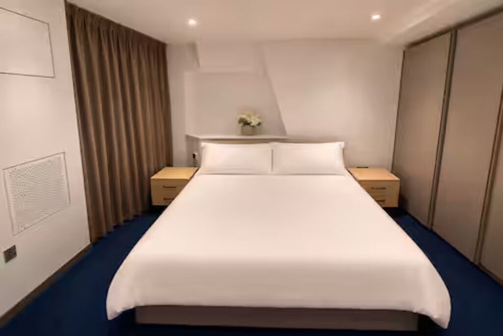A hotel room with a large bed, two bedside tables, a nightstand, a dresser, and a curtain.