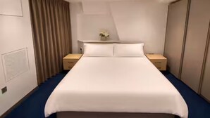 Una habitación de hotel con una cama grande, dos mesitas de noche, una mesita auxiliar, un aparador y una cortina.