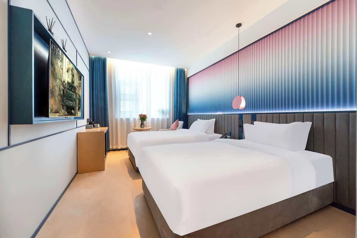 Moderni hotellihuone, jossa on kaksi sänkyä, suuri televisio ja näkymä kaupunkiin.