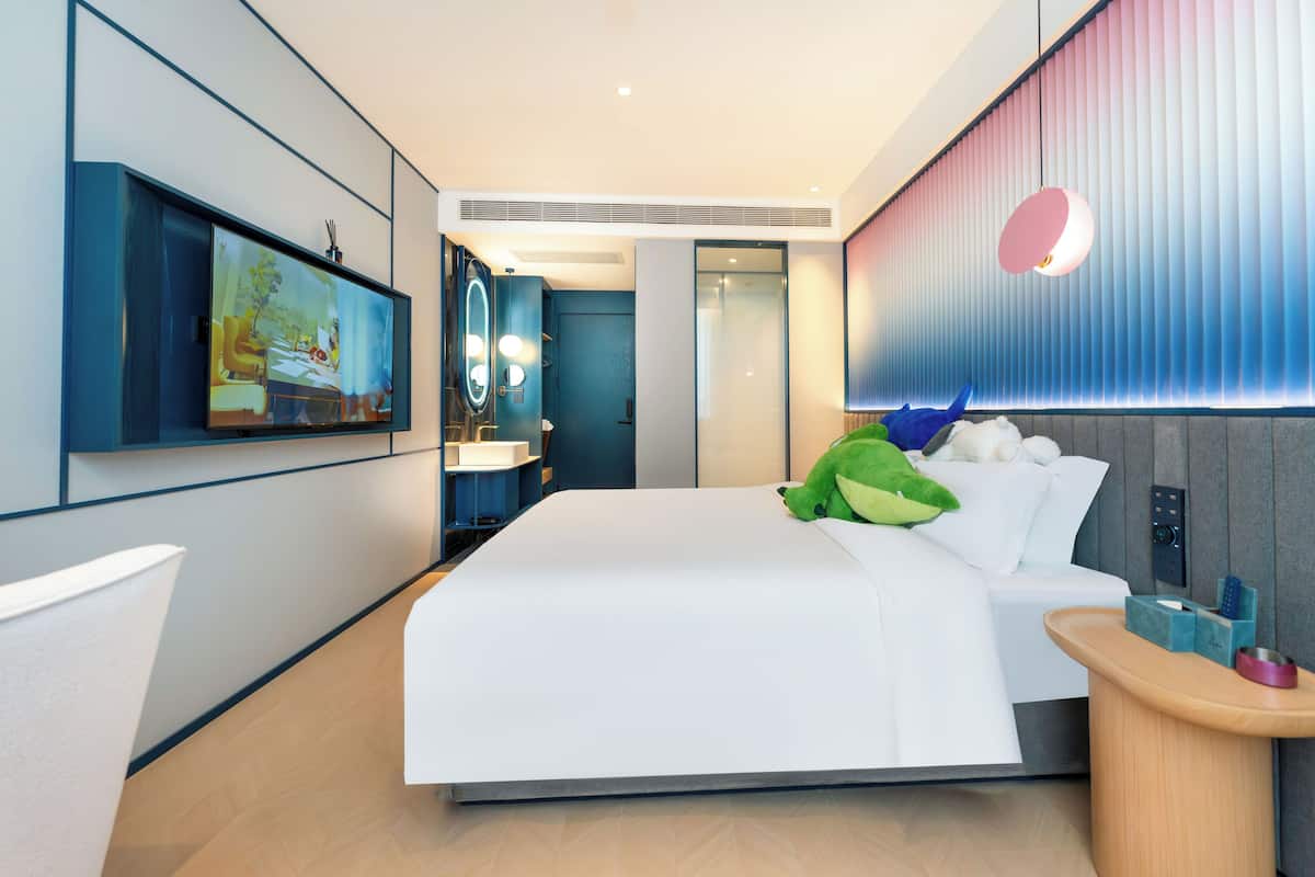 Moderni hotellihuone, jossa on suuri sänky, taulutelevisio, yöpöytä ja seinään kiinnitetty valaisin.