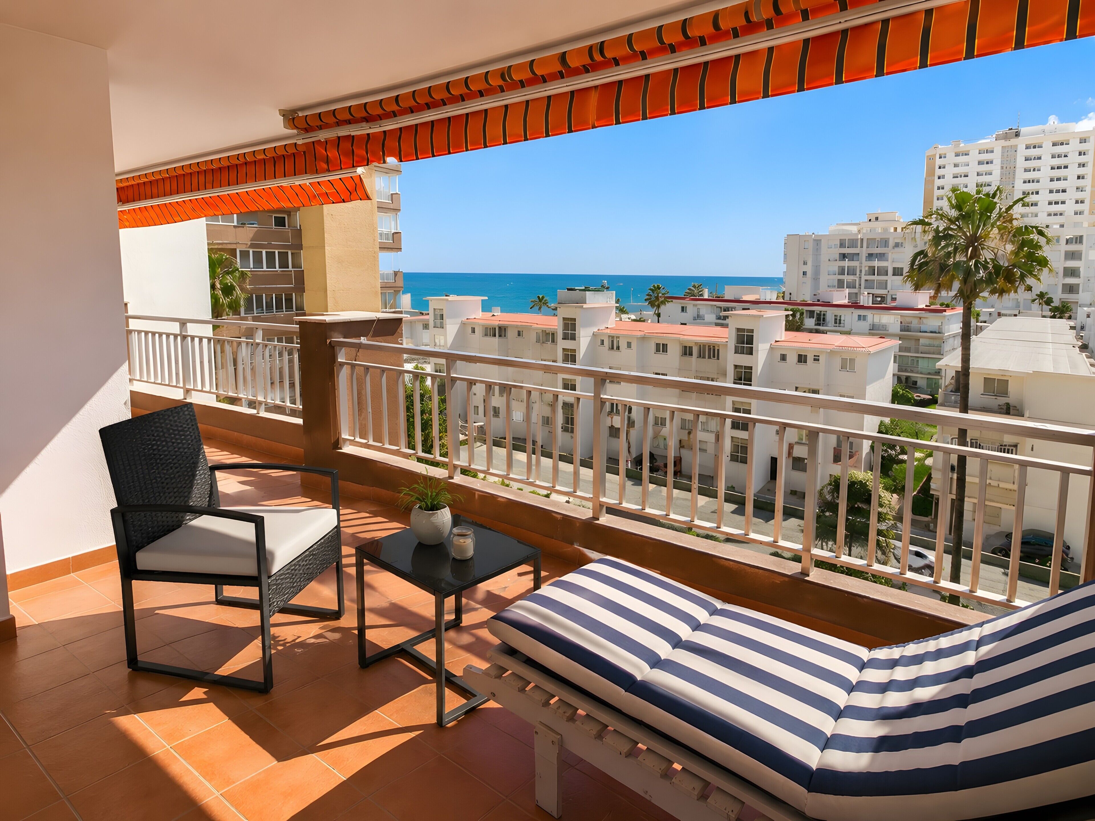 Een balkon met uitzicht op zee, een stoel, een tafeltje en een gestreept kussen.