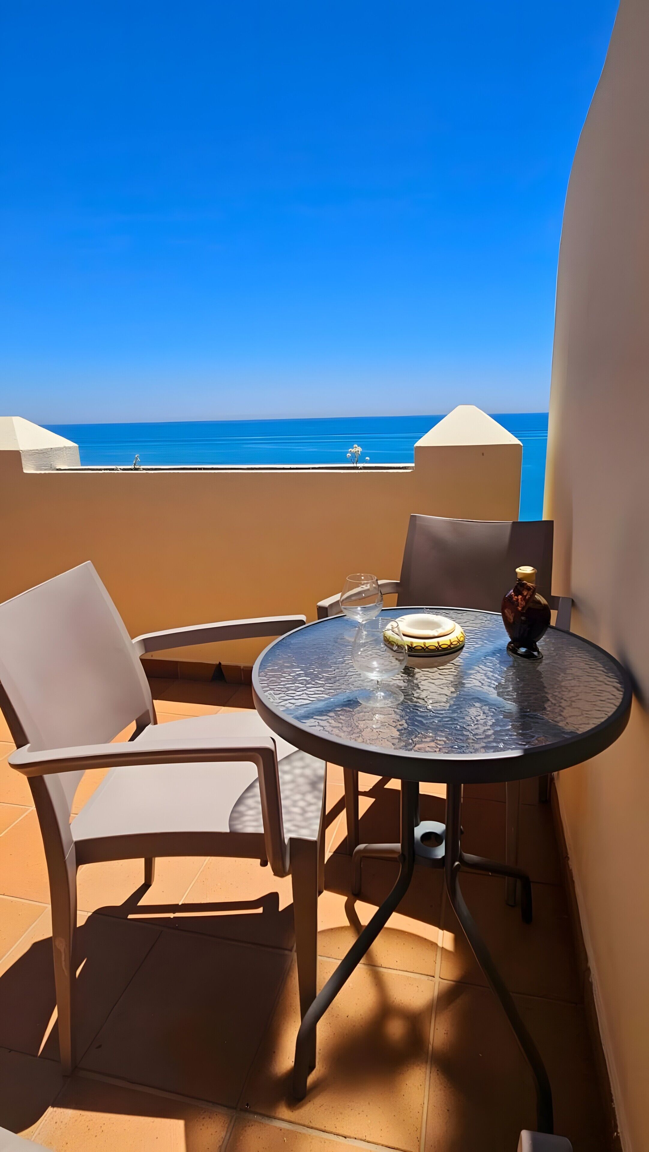 Una mesa redonda de vidrio con sillas, un adorno pequeño y vista al mar.