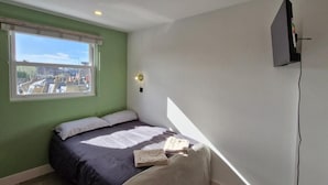 Een slaapkamer met een bed, een raam met uitzicht, een tv aan de muur en een lamp.