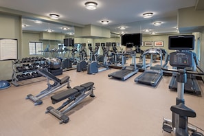 Une salle de sport équipée de divers appareils d’exercice, notamment des tapis de course, des vélos elliptiques et des poids libres.